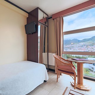 Room with a single bed and a view of the mountains and Machico on Madeira Island.